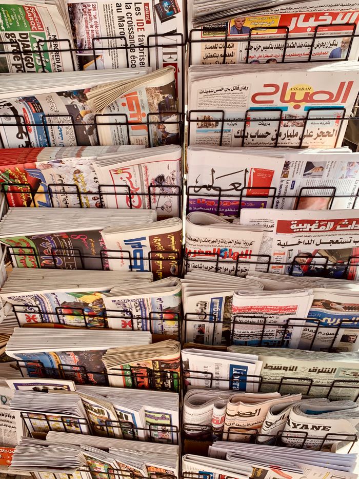 A diverse collection of newspapers in various languages displayed on a metal stand.